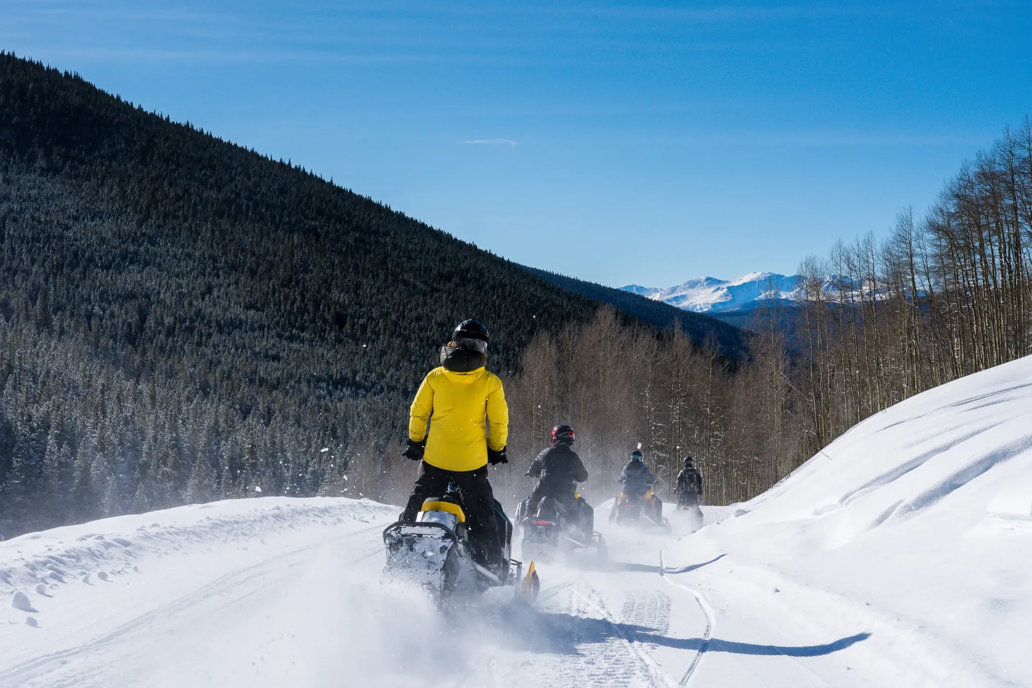 Snowmobiling group on snowy trail through forested mountains 