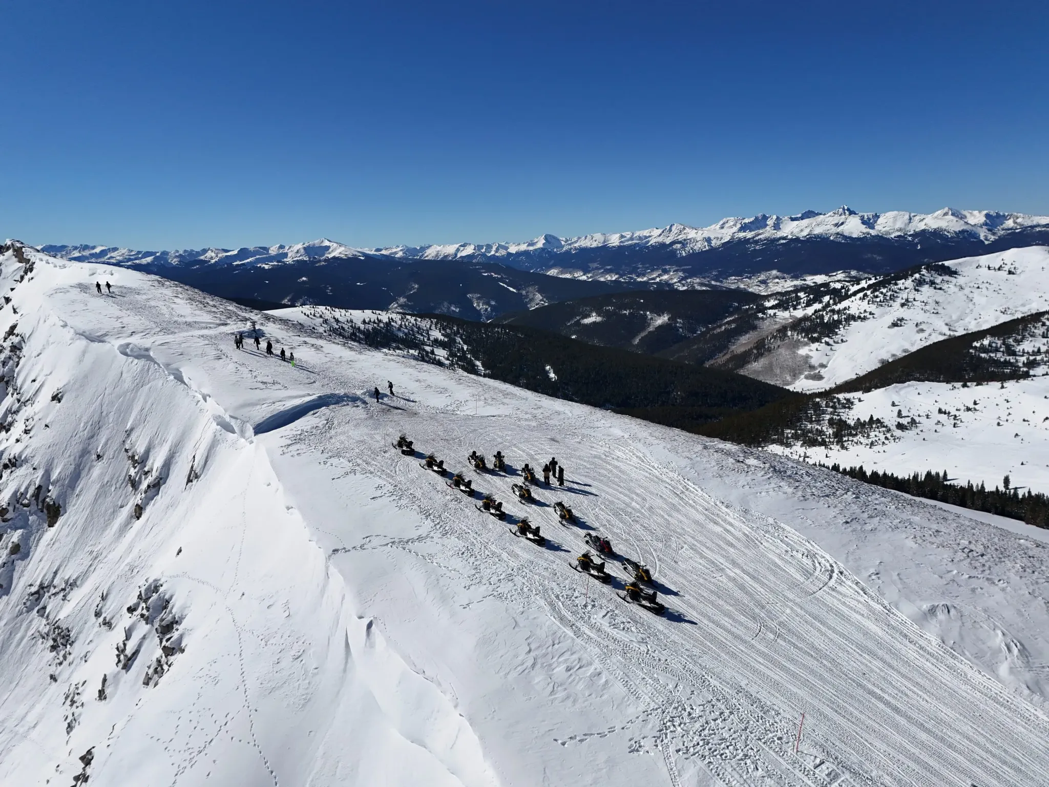 group of snowmobilers on a snowy slope taking in sweeping mountain views